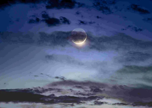 Een smalle maansikkel tussen donkere wolken
