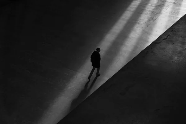 Zwart-witfoto van iemand die alleen door een schuine baan licht loopt