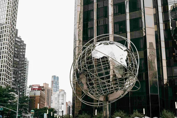 Een grote metalen wereldbol tussen hoge gebouwen in een stad