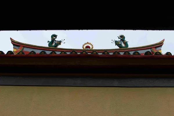 De dakrand van een tempel met twee groene draken als versiering