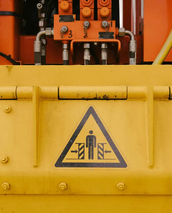 Een geel machineonderdeel met een waarschuwingsbord voor beknelling