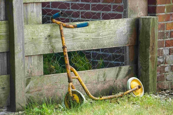Een oude, roestige step tegen een houten schutting