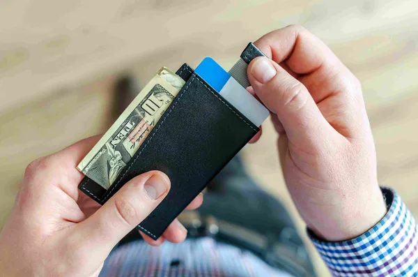 Handen met een zwarte portemonnee vol pasjes en een dollarbiljet