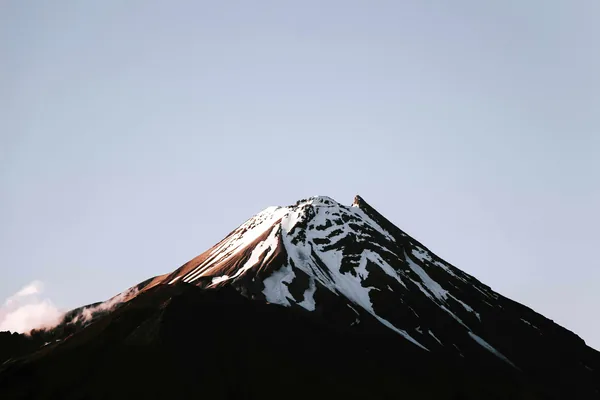 Een besneeuwde bergtop tegen een grijsblauwe lucht