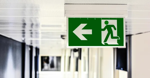 Een groen nooduitgangbord met een pijl naar links, in een gang