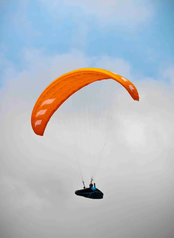 Een paraglider onder een oranje scherm in een bewolkte lucht