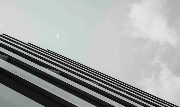 Zwart-witfoto van de maan boven de schuine rand van een gebouw