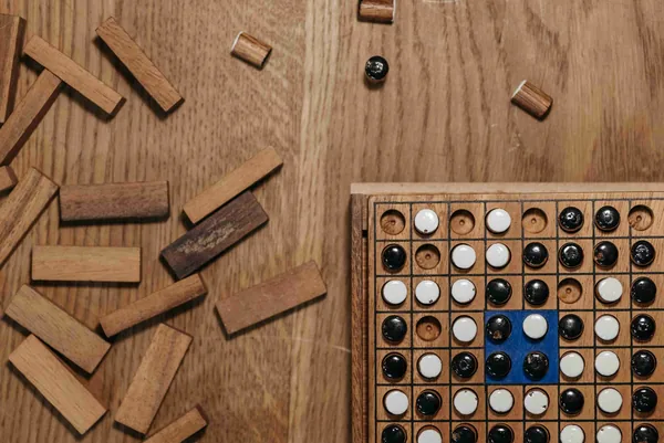 Een houten spelbord met zwarte en witte stenen, tussen losse houten blokjes