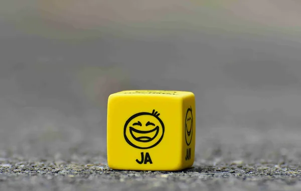 Een gele dobbelsteen met een lachend gezicht en het woord ‘ja’