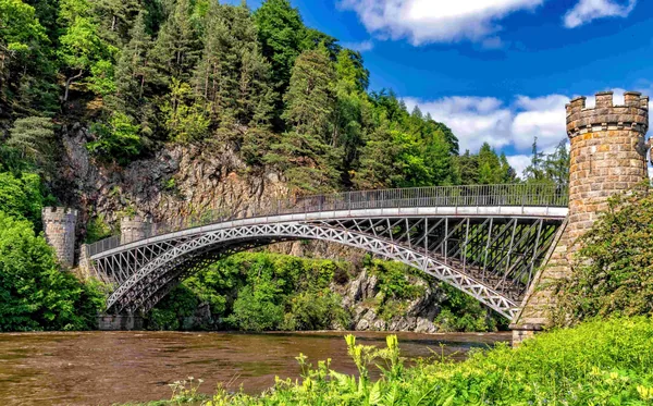 Een ijzeren boogbrug over een rivier, met een stenen torentje en bos