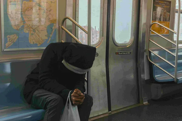 Iemand met capuchon en mondkapje zit voorovergebogen in de metro