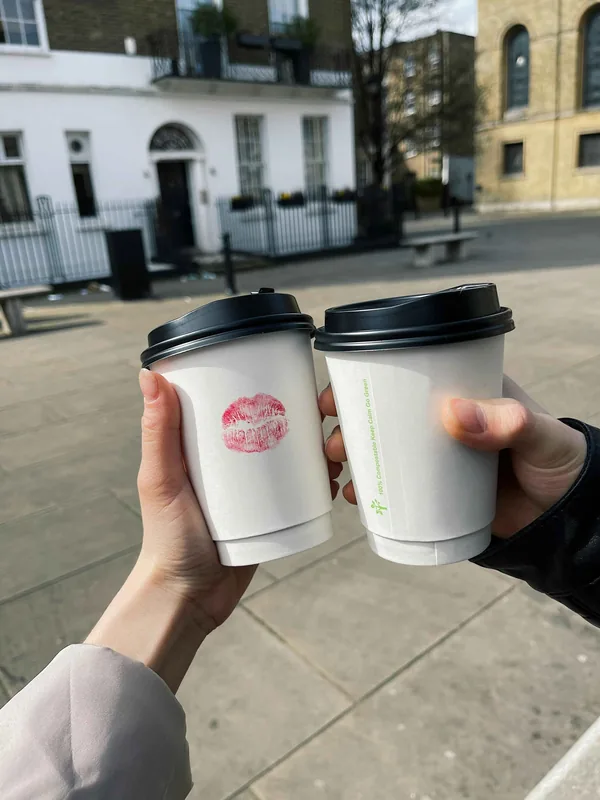 Twee handen tikken koffiebekers tegen elkaar op straat